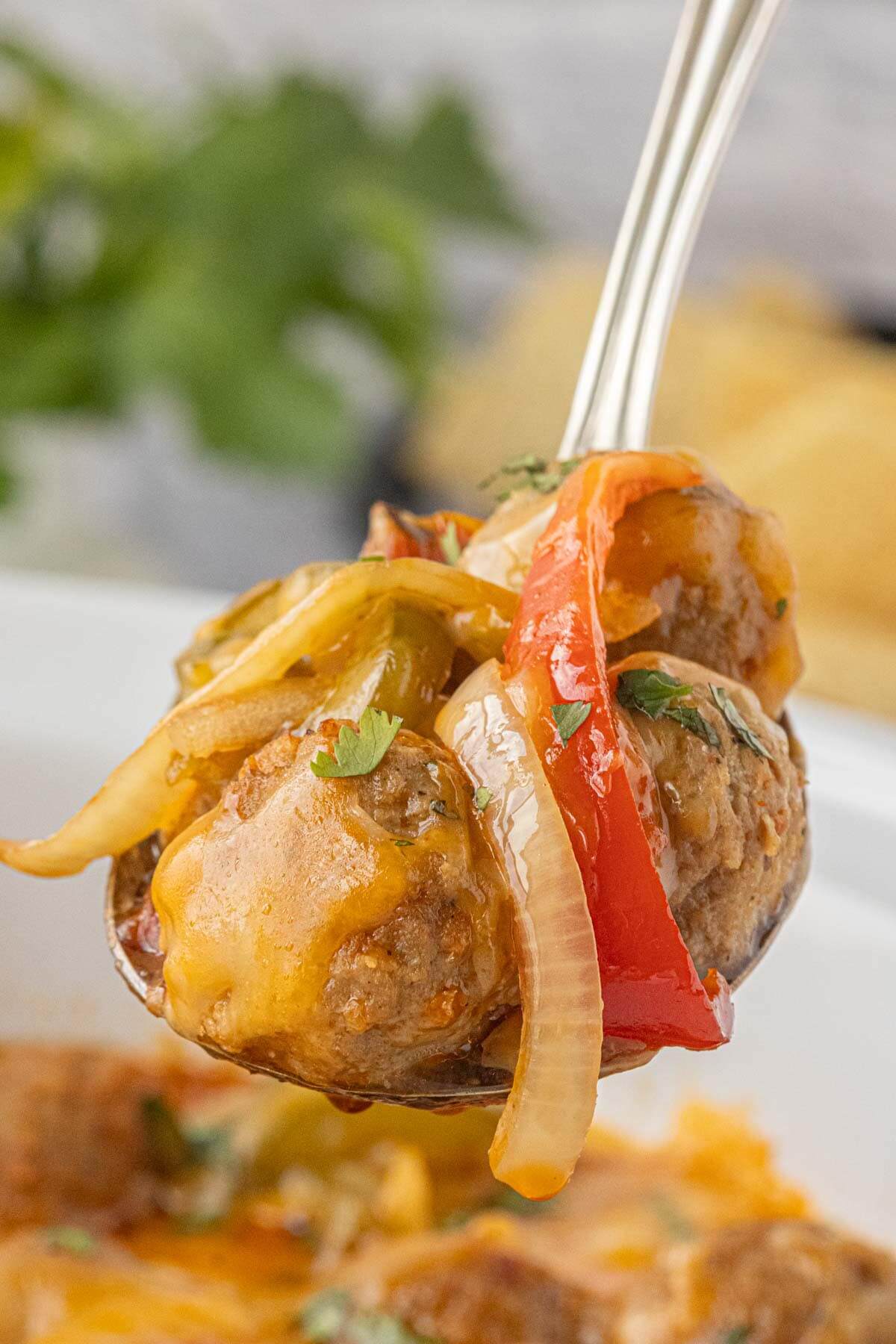 Close-up of a spoonful of meatball with melted cheese, peppers, and onions.