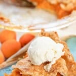 Slice of homemade apricot pie with a golden flaky crust and a scoop of vanilla ice cream on top, served on a plate with fresh apricots in the background.