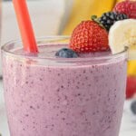Berry banana blast smoothie in a glass with a red straw, topped with fresh strawberry, banana slice, and berries, with text overlay “Berry Banana Blast Smoothie”.