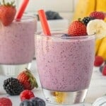 Creamy berry banana smoothie in a glass with a red straw, with fresh berries scattered around the base on a marble surface.