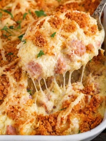 Chicken cordon bleu casserole with creamy chicken and ham, melted Swiss cheese, and a buttery cracker topping being lifted from a baking dish with a spoon.