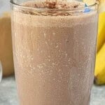 A frosty Chocolate Peanut Butter Banana Smoothie in a tall glass garnished with a slice of banana. With print overlay for Pinterest.