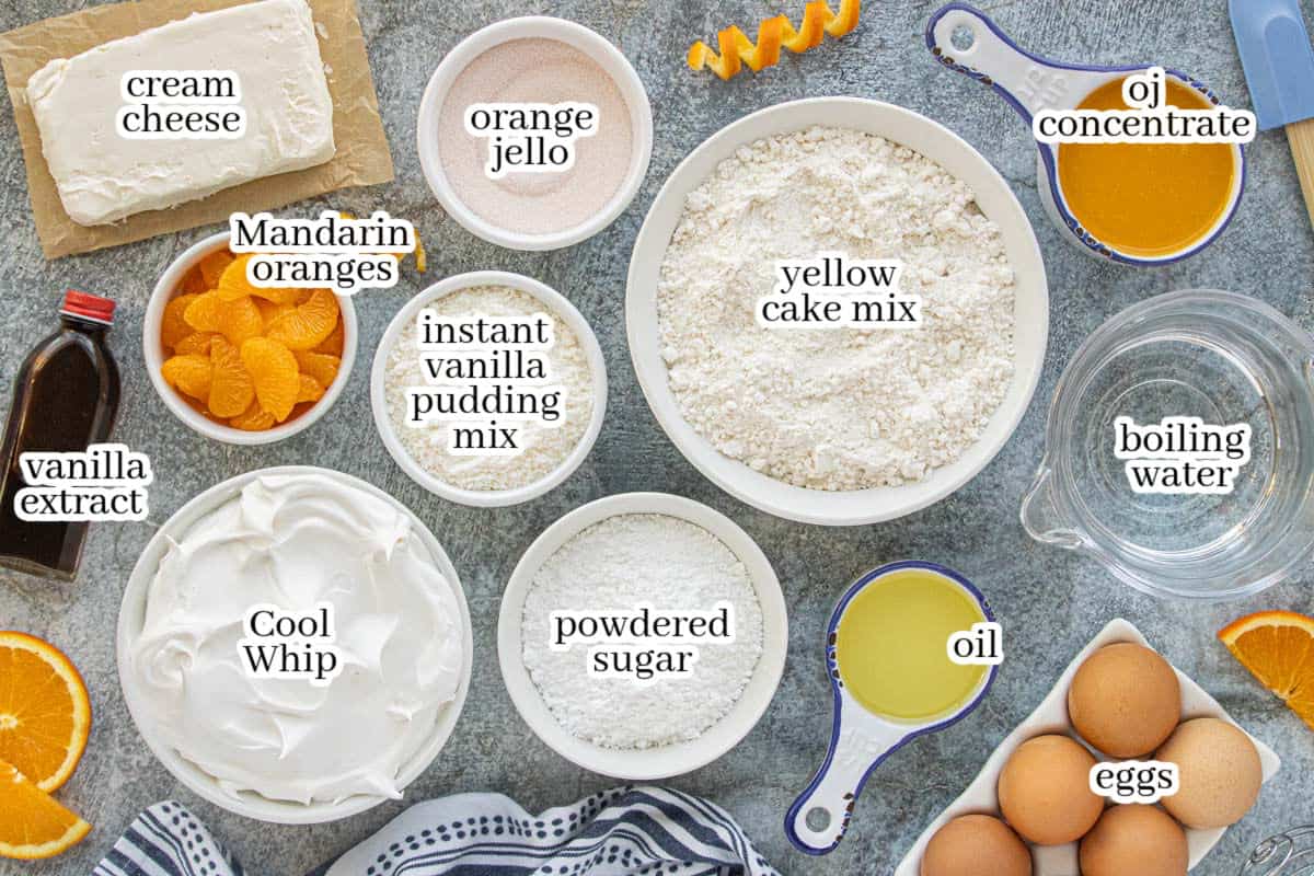Overhead view of ingredients for creamsicle poke cake including cake mix, orange gelatin, orange juice concentrate, cream cheese, Cool Whip, pudding mix, eggs, oil, powdered sugar, and mandarin oranges.