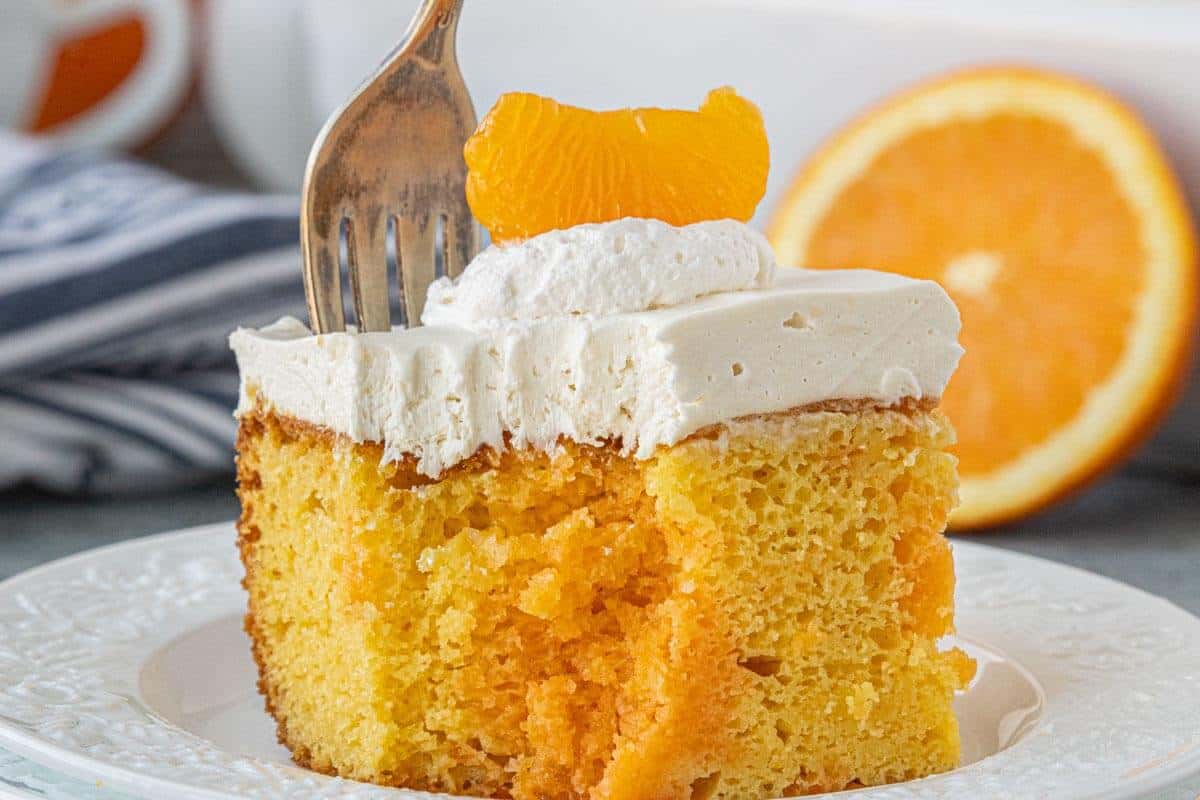 Bite taken from a slice of creamsicle poke cake on a plate with visible orange-filled pockets and whipped topping.