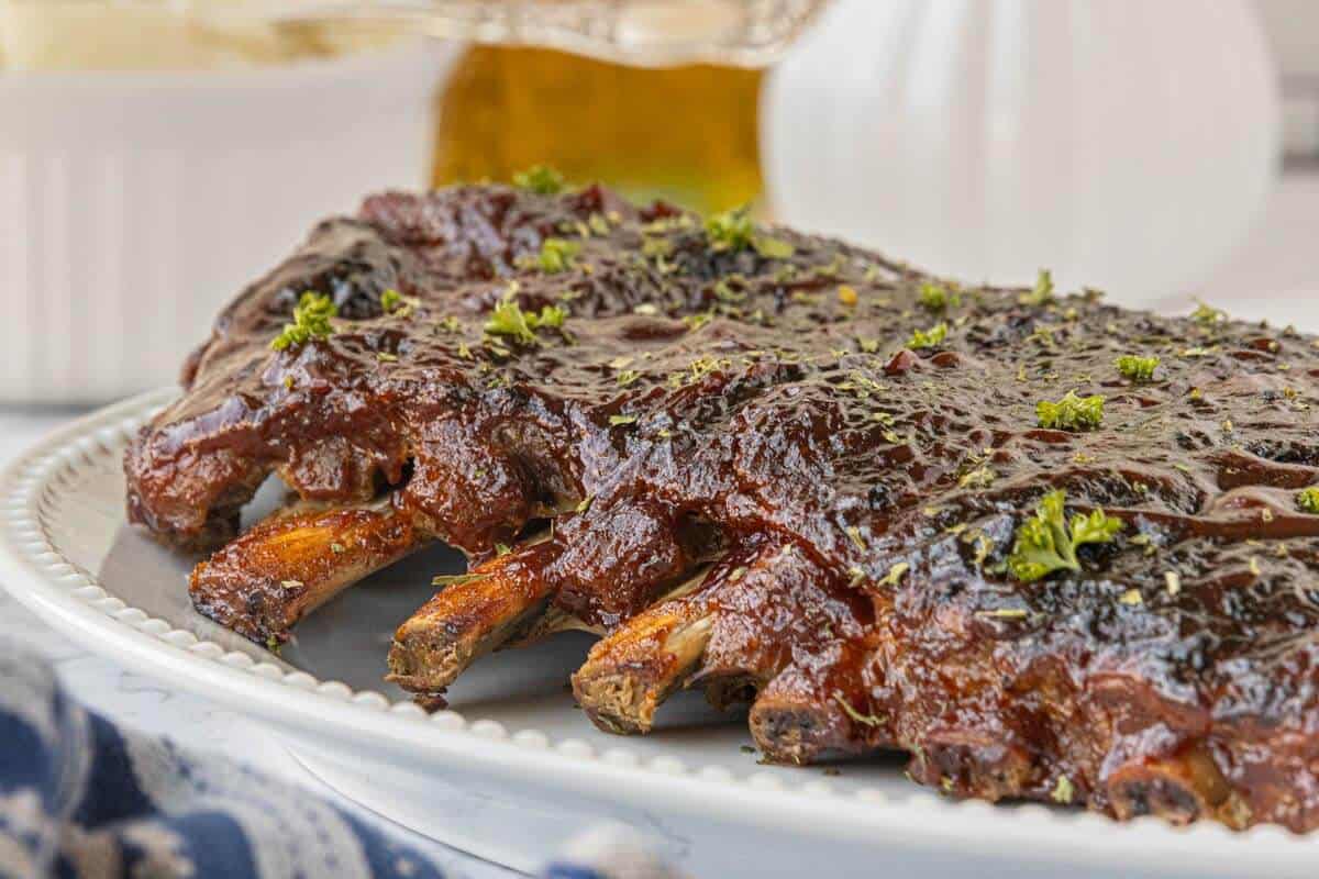 Glazed pork ribs coated in barbecue sauce on a serving platter, sprinkled with herbs.