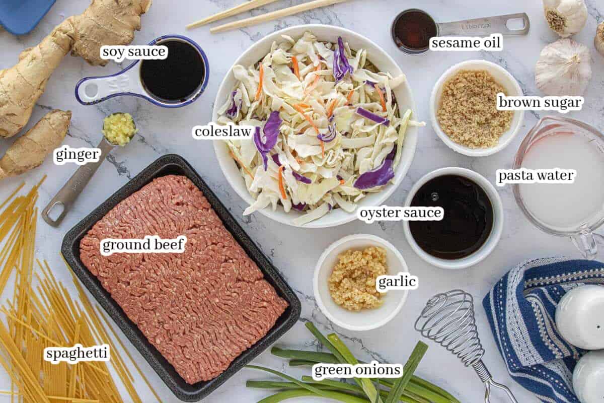 Ingredients for ground beef chow mein including spaghetti, ground beef, coleslaw mix, soy sauce, garlic, ginger, and sesame oil arranged on a countertop.