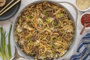 Ground beef chow mein fully mixed in a skillet with noodles, cabbage, and green onions.