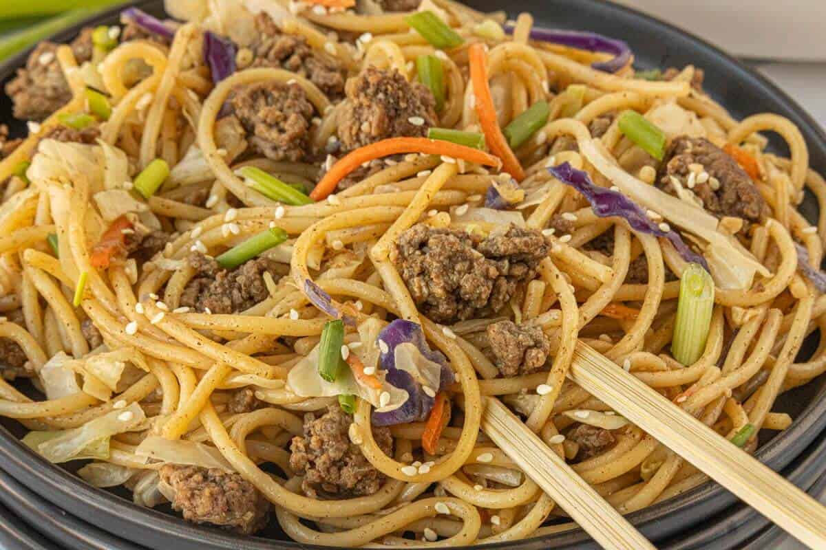 Chow mein in a bowl with browned ground beef and vegetables. With chopsticks.