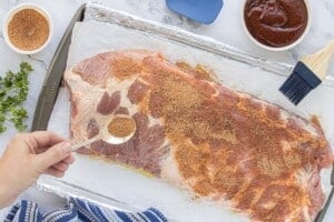 Raw pork ribs on a foil-lined baking sheet being coated with dry rub seasoning.