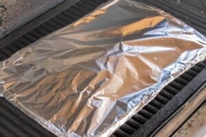 Ribs wrapped in foil cooking on a grill grate.