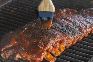 Rack of ribs on a grill as barbecue sauce is brushed over the top during grilling.
