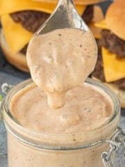 Close-up of creamy smashburger sauce on a spoon above a glass jar.