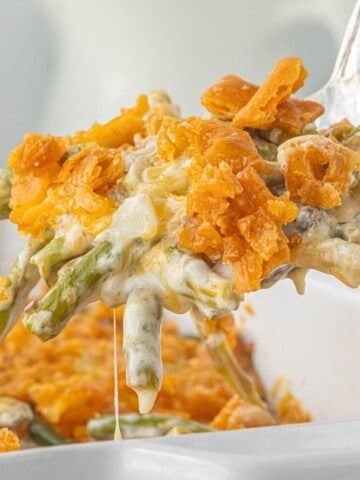 Close-up of asparagus casserole showing tender asparagus in a rich sauce with a crunchy cheese cracker topping being lifted from the casserole dish with a spoon.