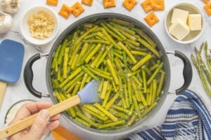 Blanched asparagus in a stockpot being stirred with a spatula.