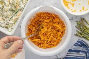 Crushed crackers, cheese and butter being stirred together with a spoon.