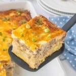 Slice of biscuits and gravy casserole with sausage, eggs, and melted cheddar cheese served from a baking dish on a black spatula.