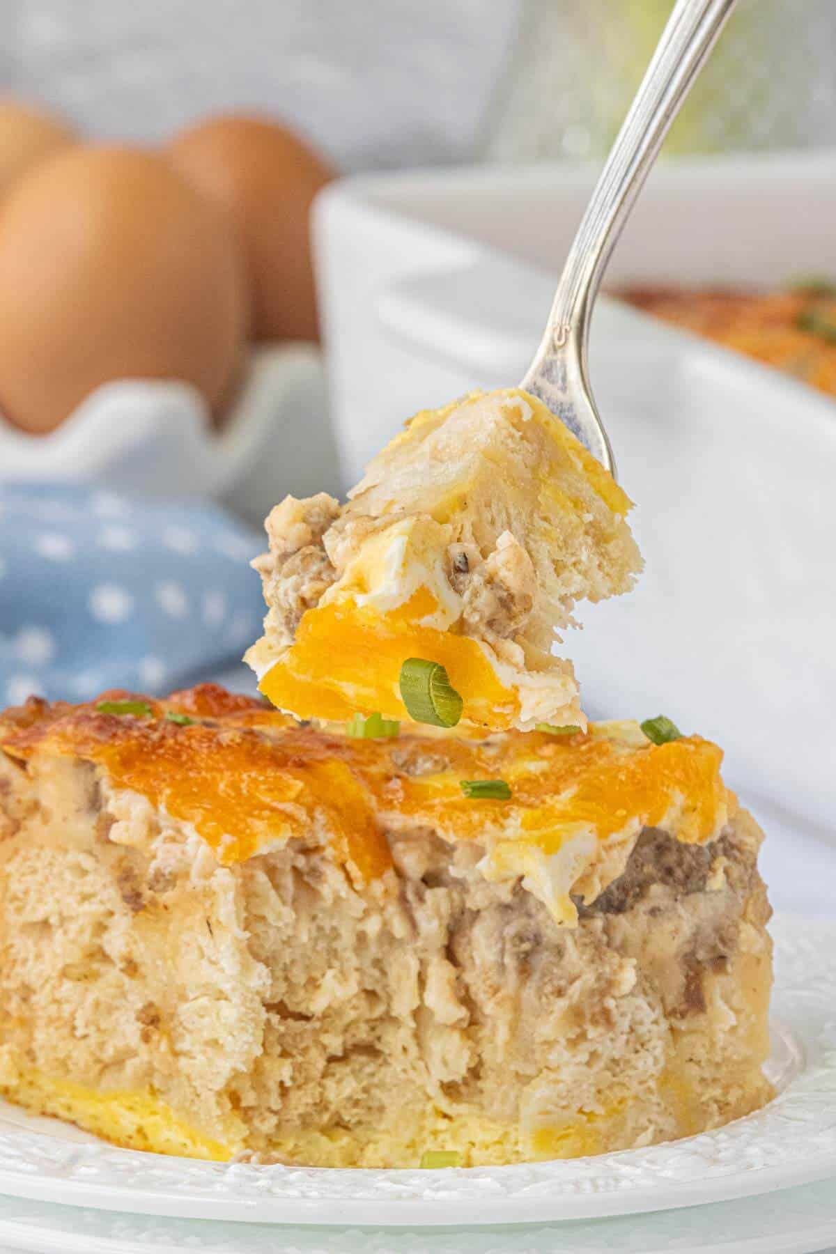 Fork lifting a bite of biscuits and gravy breakfast casserole topped with cheddar cheese and green onions.