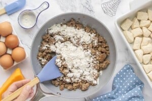 Flour sprinkled over cooked breakfast sausage in a skillet to begin making homemade sausage gravy for casserole.