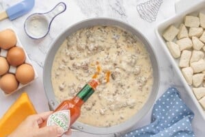 Sausage gravy in a skillet with Tabasco sauce being added for seasoning.