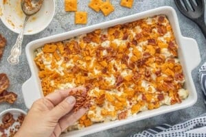 Cauliflower casserole topped with crushed crackers and crispy bacon before baking in a white casserole dish.