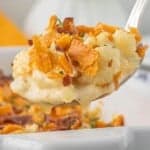 Spoonful of creamy cauliflower casserole topped with crispy bacon and crushed crackers lifted from a white baking dish.