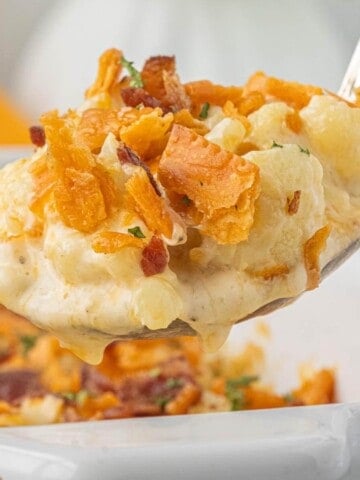 Spoonful of creamy cauliflower casserole topped with crispy bacon and crushed crackers lifted from a white baking dish.