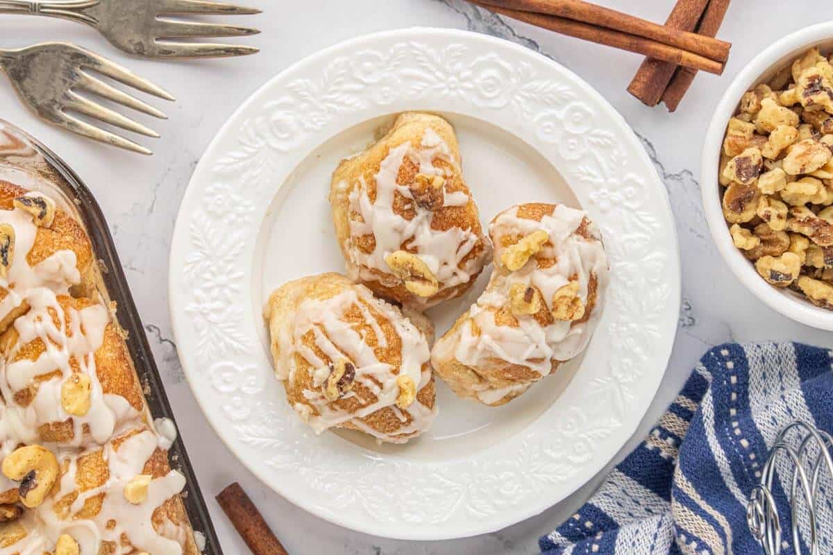 Plate of cinnamon rolls topped with glaze and walnuts, served warm.