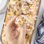 Hand holding a piece of a cinnamon roll topped with glaze and chopped nuts.