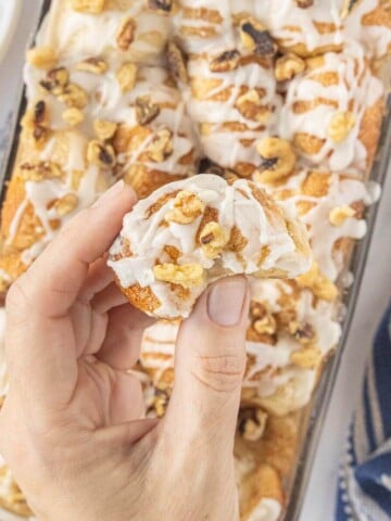 Hand holding a piece of a cinnamon roll topped with glaze and chopped nuts.