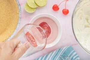 Pouring boiling water into a bowl of cherry gelatin powder to dissolve the gelatin for No-Bake Cherry Limeade Pie.
