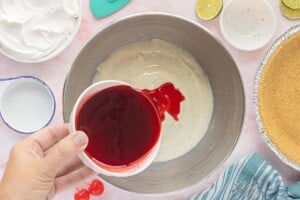 Pouring dissolved cherry gelatin into the cream cheese and lime mixture in a large mixing bowl.