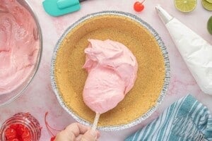 Spooning the creamy cherry limeade pie filling into a prepared graham cracker crust before chilling.