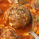 Oven baked porcupine meatballs in hearty tomato sauce garnished with fresh parsley in a casserole dish with a meatball on a spoon ready to dish up.