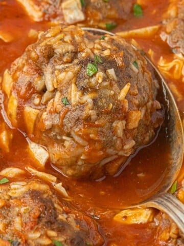 Oven baked porcupine meatballs in hearty tomato sauce garnished with fresh parsley in a casserole dish with a meatball on a spoon ready to dish up.