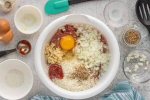 Ground beef, rice, onion, egg, ketchup, garlic, and seasonings combined in a large mixing bowl.