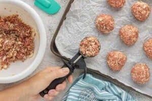 Raw porcupine meatballs portioned with an ice cream scoop onto a parchment-lined baking sheet.
