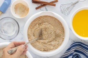 Mix cinnamon sugar in a white bowl with a spoon, surrounded by baking ingredients on the counter.