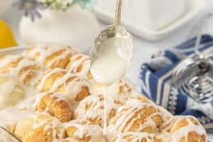 Drizzle lemon glaze over freshly baked pull-apart cinnamon rolls in a glass baking dish.