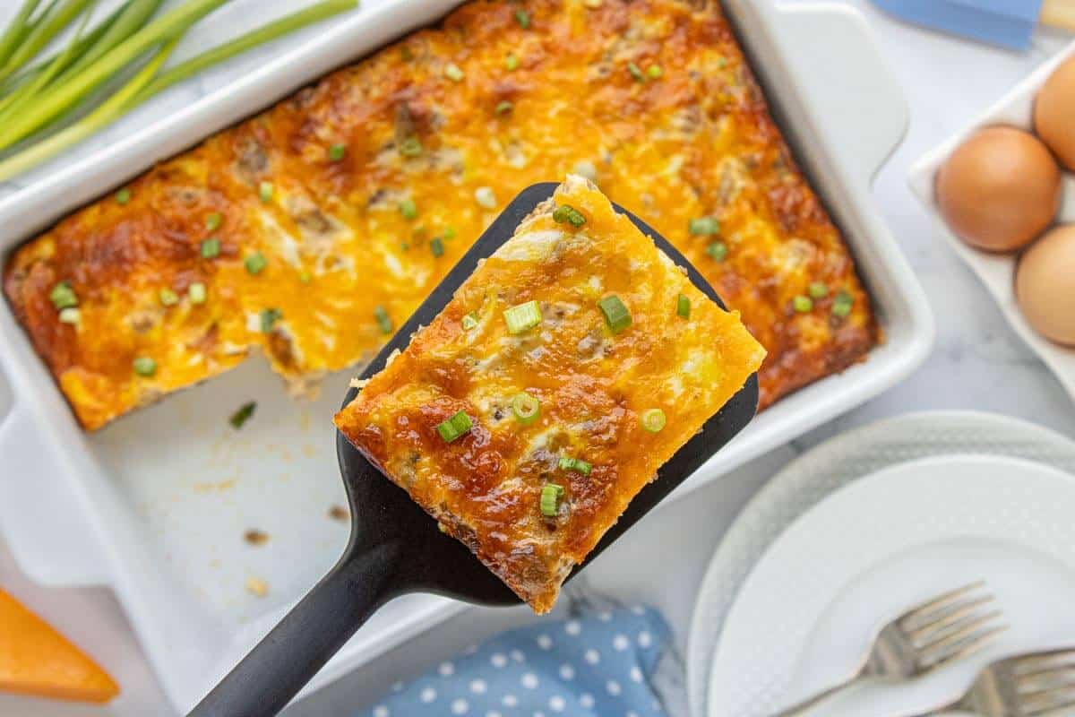Slice of southern biscuits and gravy casserole on a spatula. It's topped with melted cheese and green onions ready to serve.