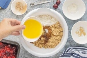 Pouring melted butter over oats, flour, brown sugar, cinnamon, and vanilla to make the crisp topping.
