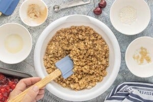 Mixing the buttery oat topping until the ingredients are evenly combined and crumbly.