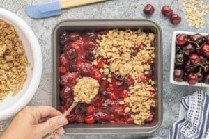 Sprinkling the oat crumble evenly over the cherry filling before baking.
