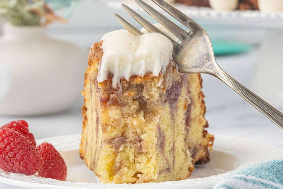 Slice of White Chocolate Raspberry Bundt Cake on a plate with a fork showing raspberry swirls and cream cheese frosting.