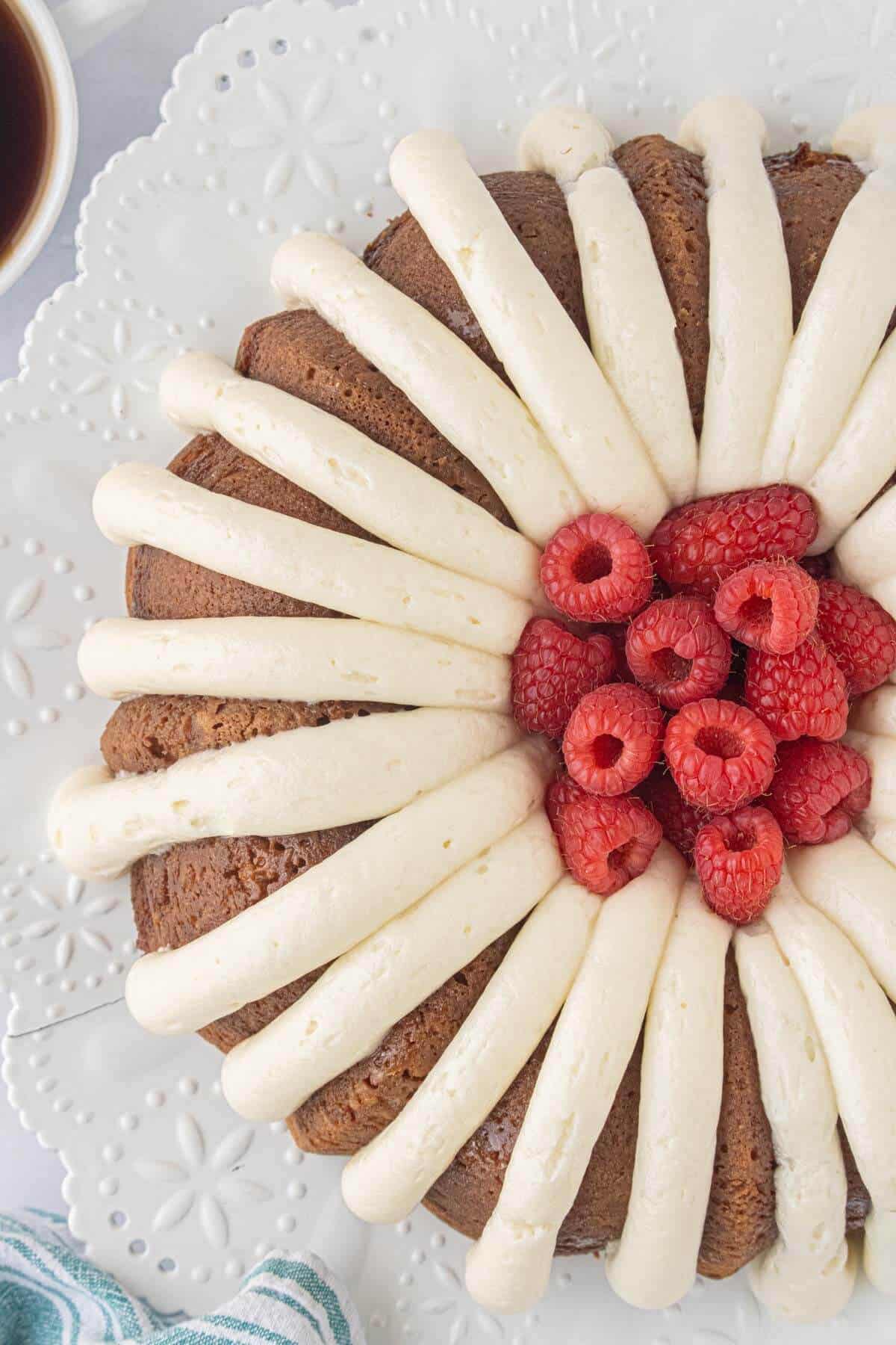 Overhead view of Copycat White Chocolate Raspberry Bundt Cake decorated with cream cheese frosting and fresh raspberries.