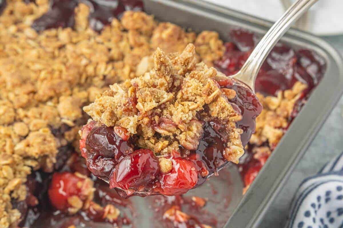 Serving homemade cherry crisp lifted from the baking dish, showing the thick cherry filling and crisp oat topping.