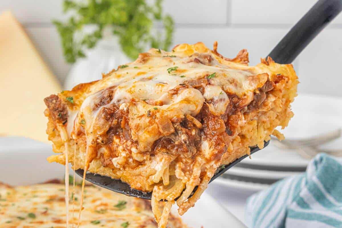 Spatula serving a generous portion of baked spaghetti pie casserole topped with gooey melted cheese and savory meat sauce.