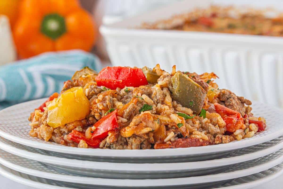 Serving of cheesy bell pepper casserole with seasoned ground beef, rice, and red, yellow, and green bell peppers on a white plate.