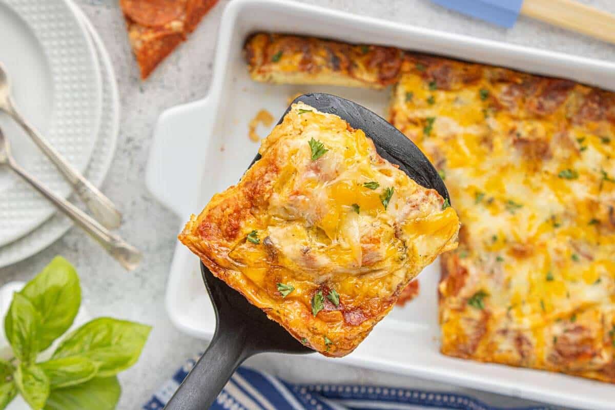 Overhead view of Leftover Pizza Breakfast Casserole with a cheesy slice lifted from the baking dish.