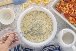 Whisking eggs, milk, and seasonings in a white bowl.