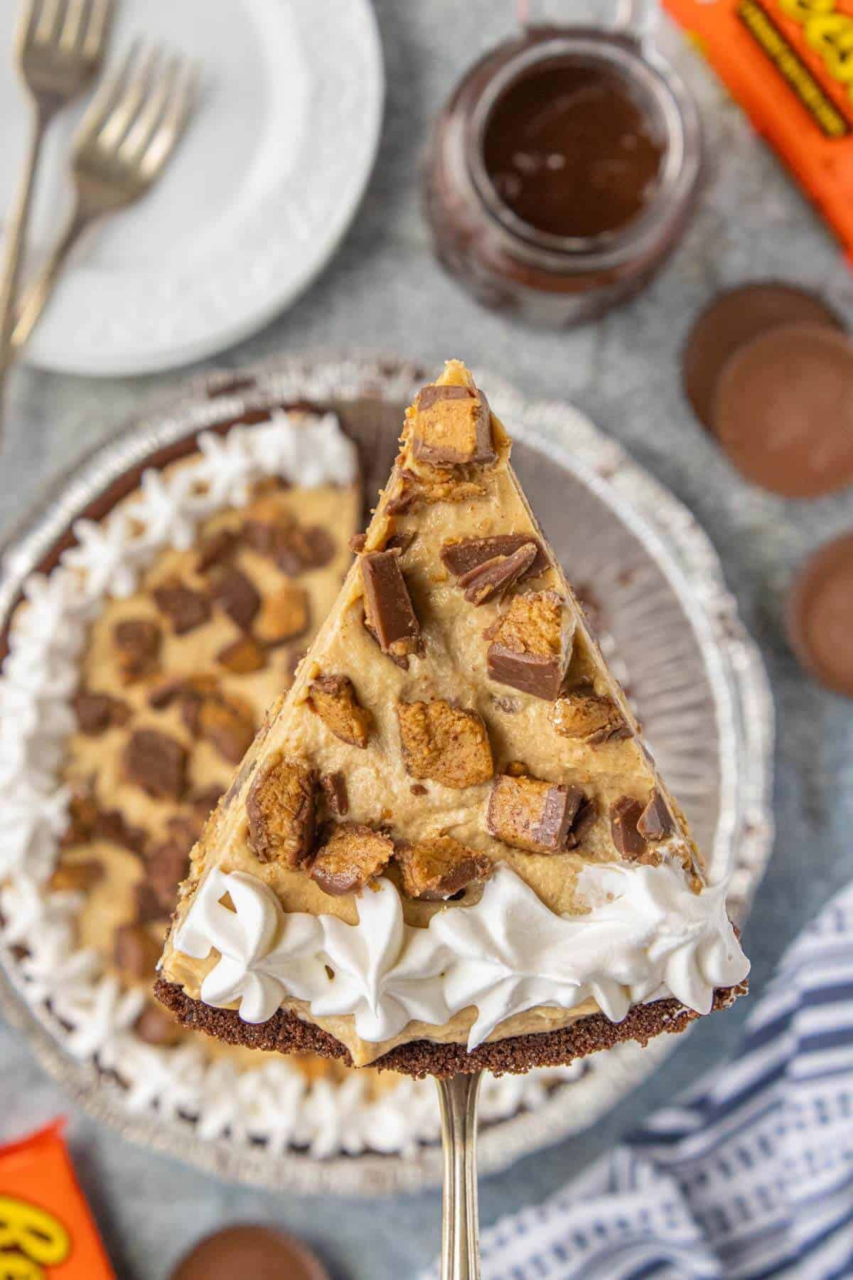 Overhead view of a slice of no-bake peanut butter cup cheesecake topped with chopped peanut butter cups and whipped topping on a pie server.